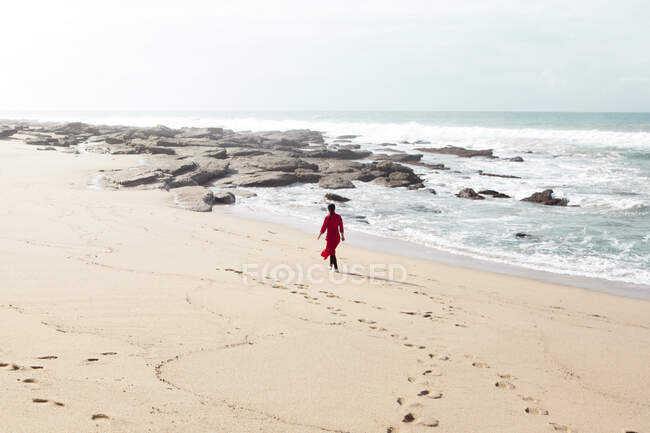 Mujer vestida de rojo, caminando por la playa, Sudáfrica - foto de stock