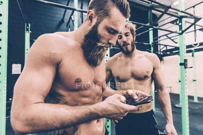 Homme cross trainer lecture smartphone mise à jour dans la salle de gym — Photo de stock