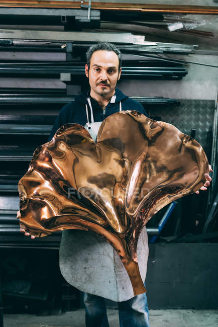 Portrait of male metalworker holding copper product, forge storeroom — Stock Photo