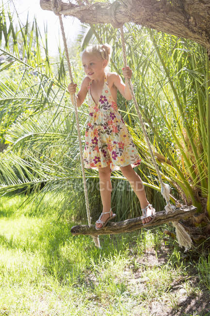 Chica de pie balanceándose en el árbol swing en el jardín - foto de stock