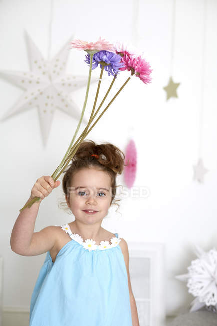 Girl holding up gerberas against white wall with stars — Stock Photo