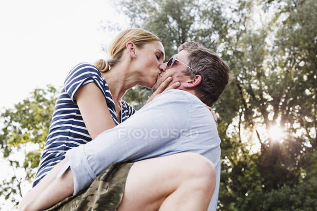 Baixo ângulo de visão de casal compartilhando beijo apaixonado no parque — Fotografia de Stock
