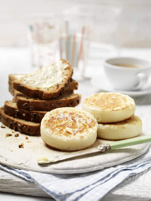 Crumpets e pão integral semeado com manteiga na tábua de cortar — Fotografia de Stock