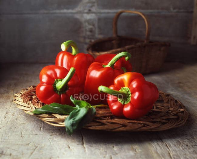 Four red peppers on vintage wicker basket on table — Stock Photo
