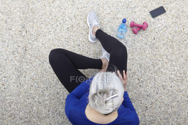 Mature woman sitting outdoors, hand weights, water and smartphone beside her, elevated view — Stock Photo