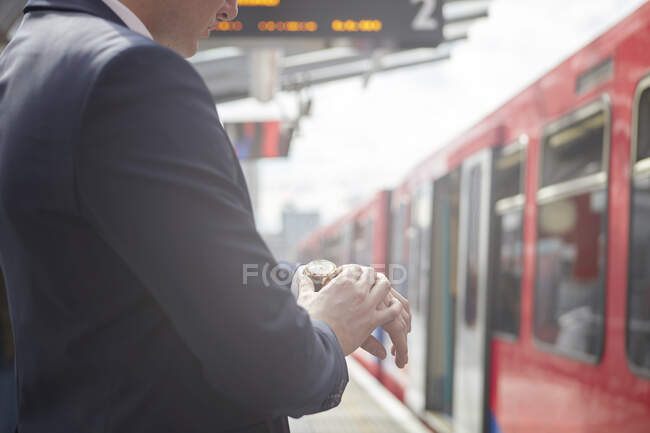 Recorte de hombre de negocios comprobando reloj en la plataforma ferroviaria, Londres, Reino Unido - foto de stock