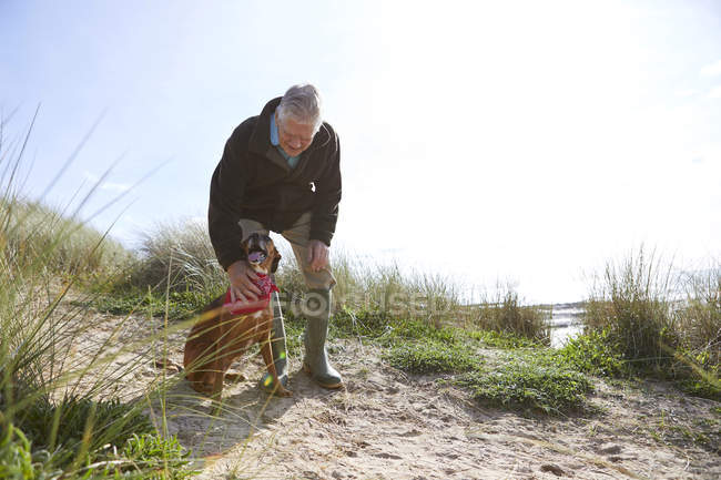 Man stroking pet dog on sand dunes, Constantine Bay, Cornwall, UK — Stock Photo