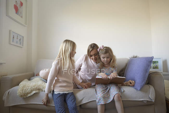 Mitte erwachsene Frau und Töchter lesen Bilderbuch auf dem Sofa — Stockfoto