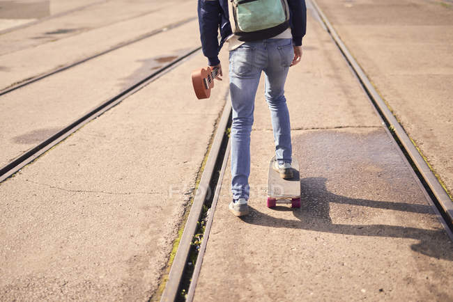 Junger Mann skateboardet zwischen Straßenbahnlinien, Rückansicht, Tiefschnitt — Stockfoto