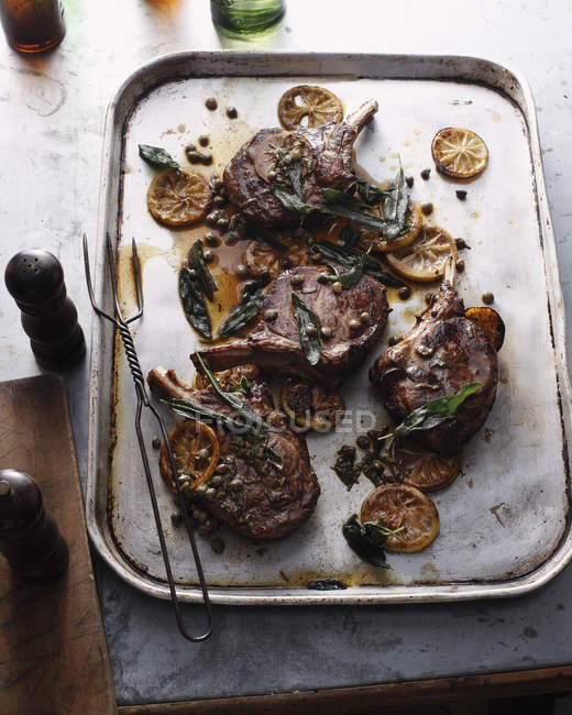 Roasted cowboy steaks with lemon slices and herbs on baking tray — Stock Photo
