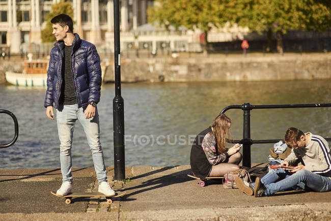 Three friends fooling around beside river, young man on skateboard, Bristol, UK — Stock Photo