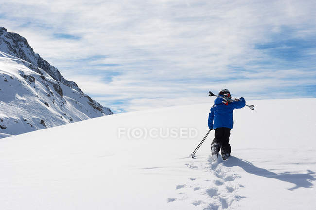 Criança carregando esquis na montanha nevada — Fotografia de Stock
