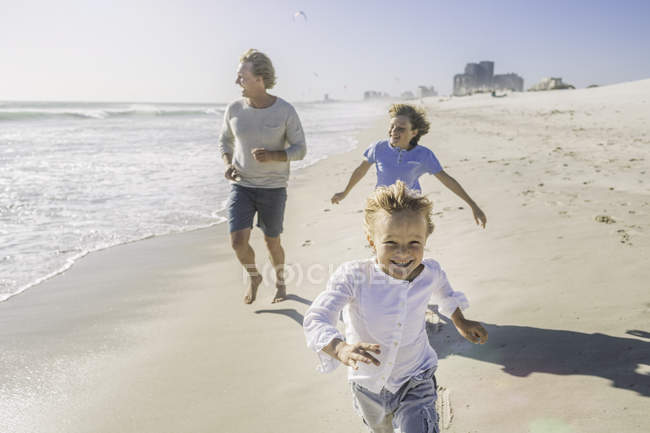 Padre e figli che corrono sulla spiaggia — Foto stock