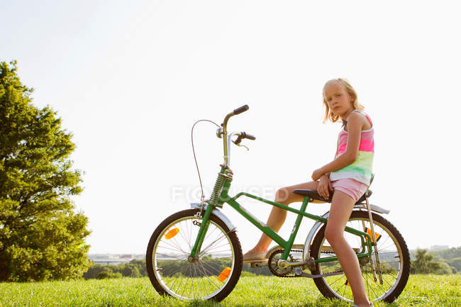Menina sentada na bicicleta na grama — Fotografia de Stock