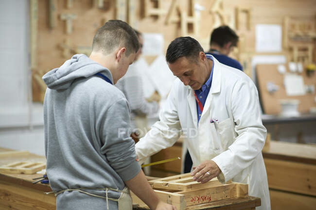 Professor do sexo masculino demonstrando medição para adolescente estudante de carpintaria em oficina universitária — Fotografia de Stock