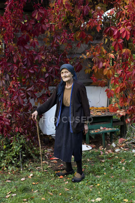 Portrait of senior woman with walking stick standing in autumn garden — Stock Photo