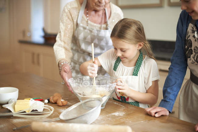 Femme âgée et petites-filles brassant le mélange de biscuits dans un bol — Photo de stock