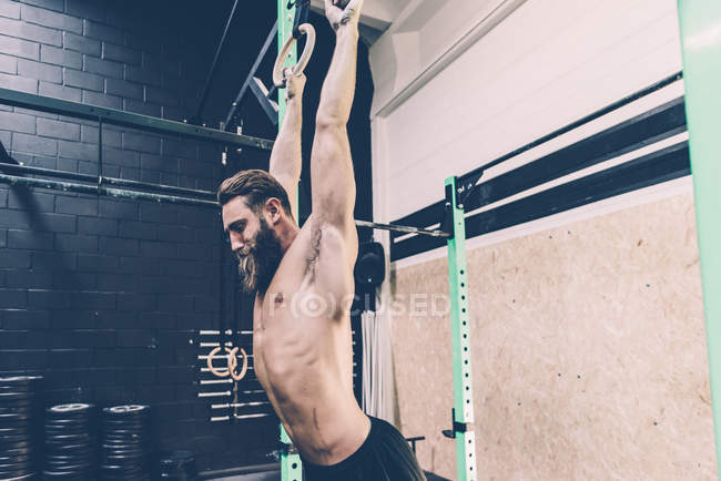 Young male cross trainer hanging from exercise rings in gym — Stock Photo