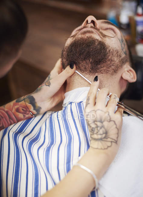 Парикмахер бреет бороду клиенту — стоковое фото