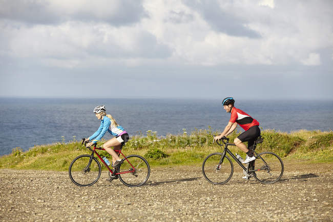 Велогонщики едут по гравийной дороге с видом на океан — стоковое фото