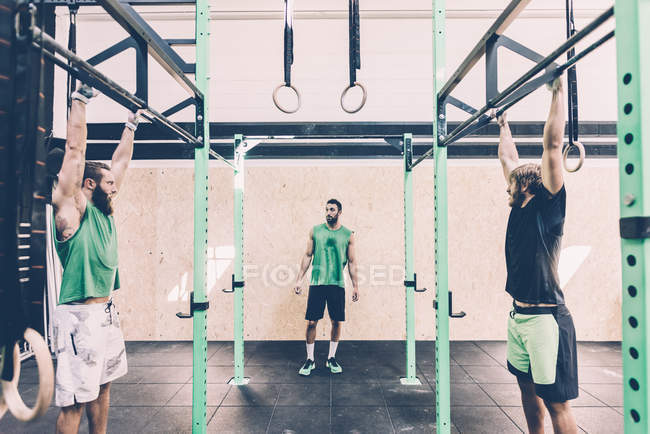 Deux entraîneurs masculins s'entraînent sur le bar d'exercice dans la salle de gym — Photo de stock