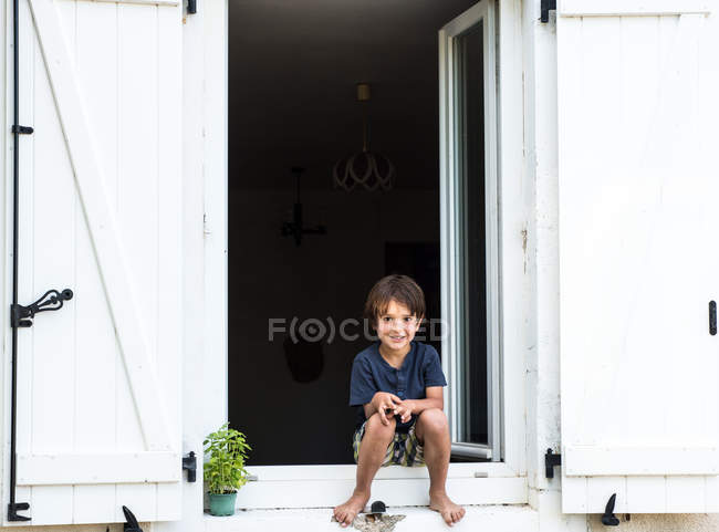 Retrato del niño sentado en la puerta del apartamento de vacaciones, Francia - foto de stock
