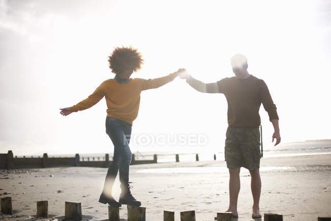 Мужчина помогает женщине балансировать на деревянных пнях на пляже — стоковое фото