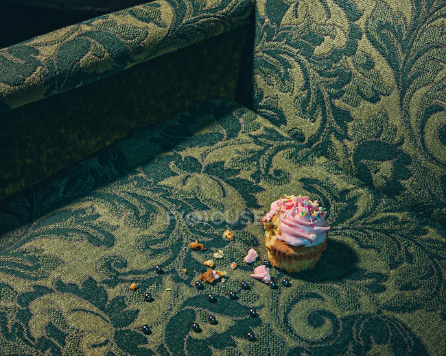 Cupcake and crumbs on armchair surface — Stock Photo