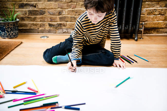Boy sitting on floor drawing on large paper — Stock Photo