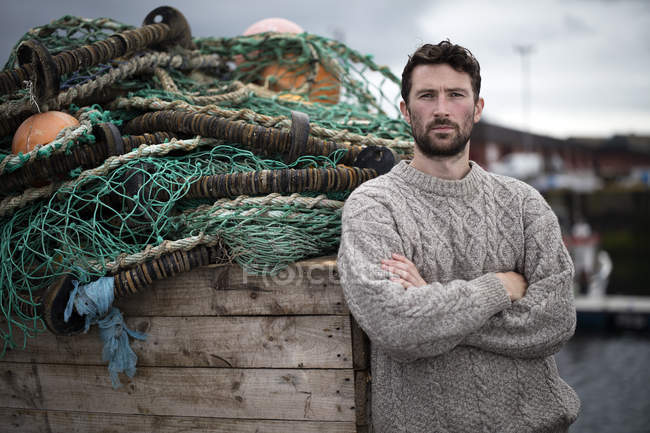 Retrato de un joven pescador apoyado en una caja de redes de pesca en el puerto de Fraserburgh, Escocia - foto de stock