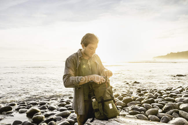 Hombre buscando mochila en la playa en Juan de Fuca Provincial Park, Vancouver Island, British Columbia, Canadá - foto de stock