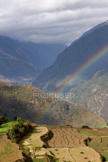 Arco-íris sobre o vale rural da montanha à luz do sol — Fotografia de Stock