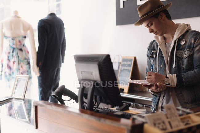 Junge männliche Verkäuferin steht hinter Theke und macht sich Notizen — Stockfoto