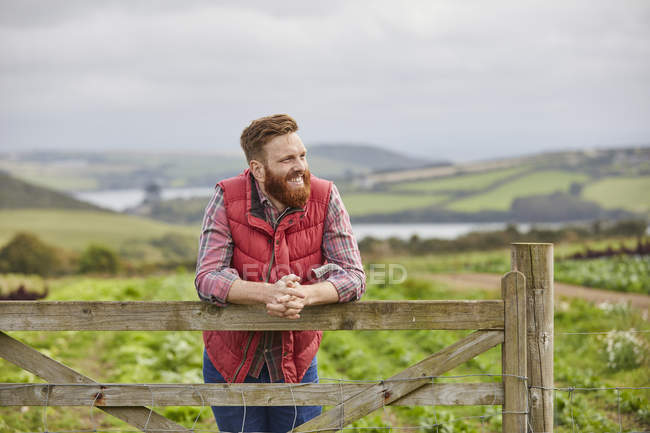 Hombre de pie en la granja apoyado contra la puerta y mirando hacia otro lado - foto de stock