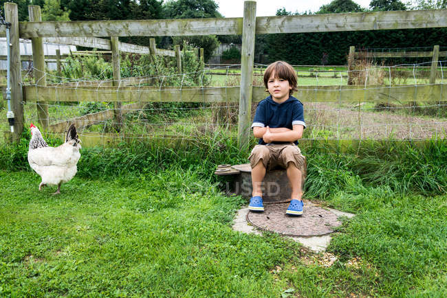 Niño sentado en la granja con pollo - foto de stock