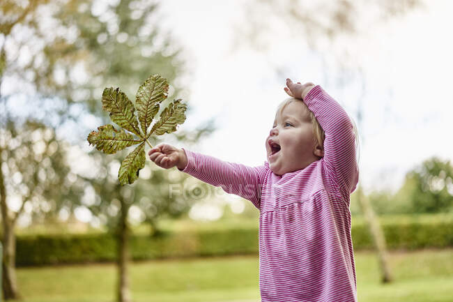 Bebê menina segurando folha olhando para longe — Fotografia de Stock
