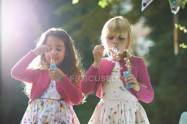 Duas meninas bonitos soprando bolhas no jardim — Fotografia de Stock