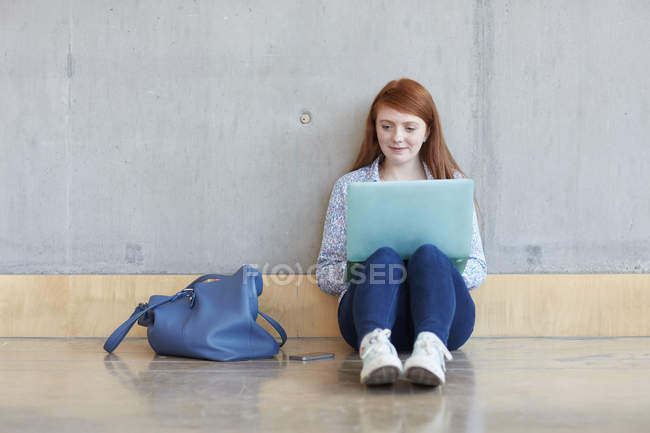 Молодая студентка, сидящая на полу с ноутбуком в колледже высшего образования — стоковое фото