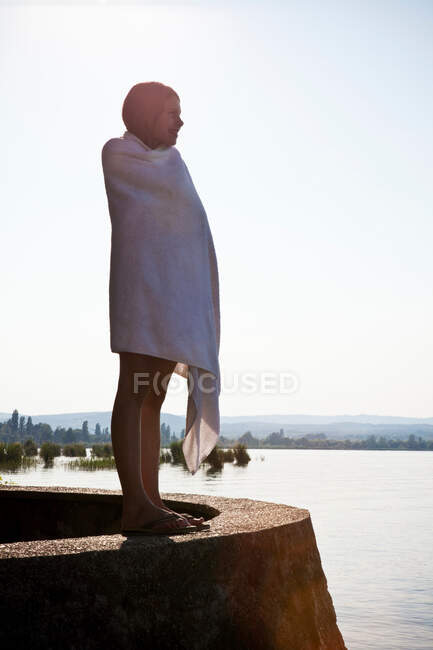 Молода дівчина, загорнута в рушник біля озера — стокове фото