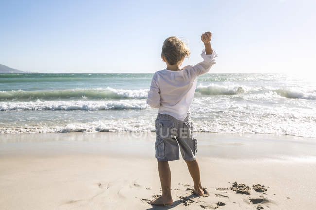 Visão traseira de comprimento total do menino na praia jogando pedras no oceano — Fotografia de Stock
