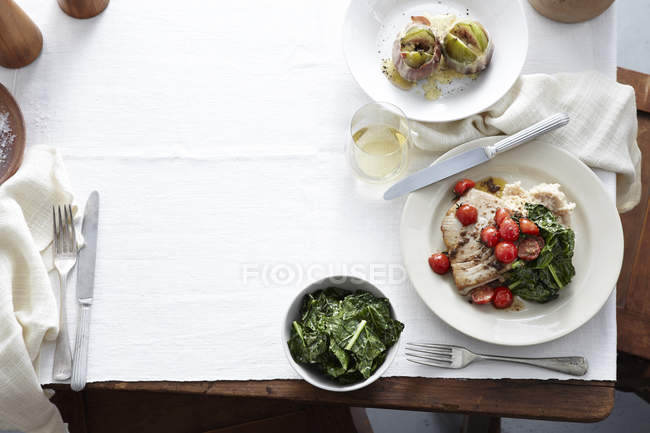 Mesa con plato de higos envueltos en jamón, espinacas, tomates cherry, filete de atún y alcaparras - foto de stock