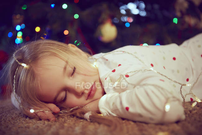Девушка в огнях спит на полу на Рождество — стоковое фото