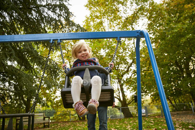Father pushing daughter on playground swing — Stock Photo