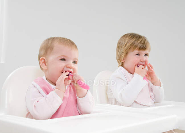 Two baby sisters in high chairs. — Stock Photo