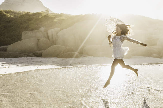 Femme sautant en plein air avec parasol sur une plage ensoleillée, Cape Town, Afrique du Sud — Photo de stock