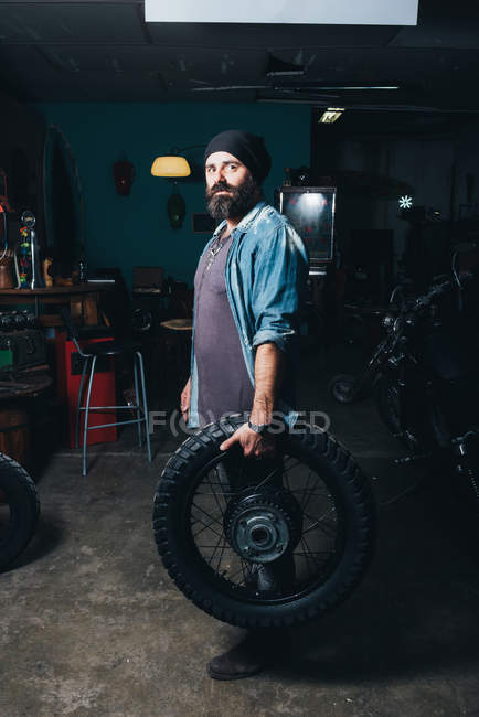 Portrait of mature man, in garage, holding motorcycle tire — Stock Photo