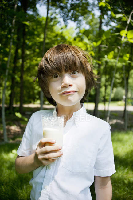 Menino na floresta bebendo milkshake e puxando uma cara — Fotografia de Stock