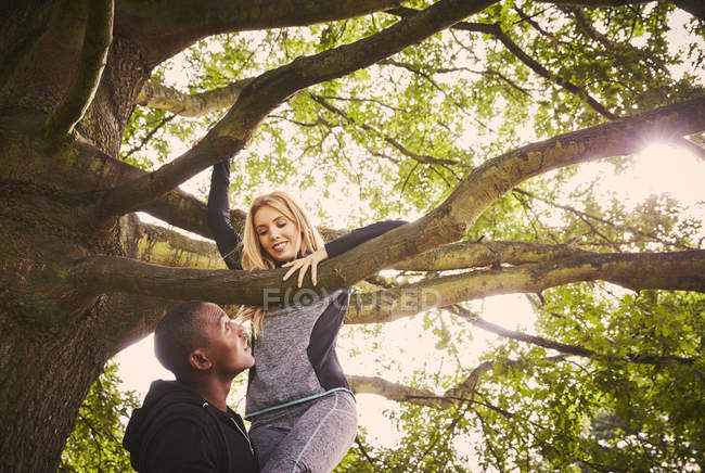 Personal trainer lifting young woman to climb park tree — Stock Photo