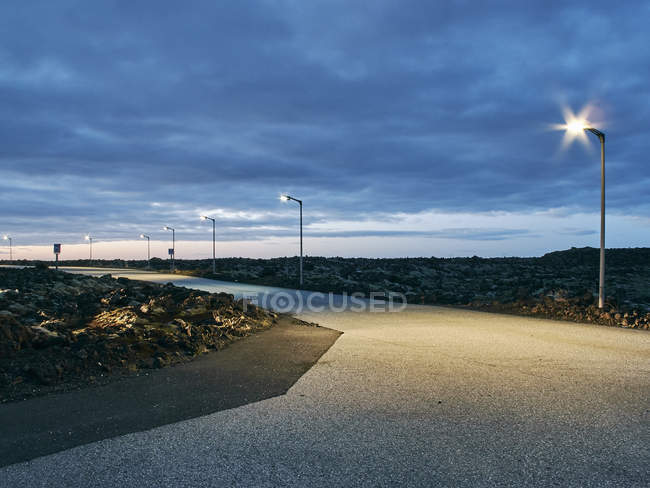 Road and street lamps at dusk with cloudy sky — Stock Photo