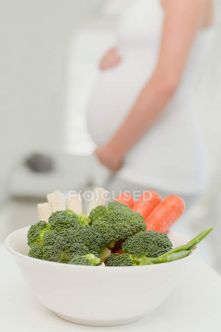 Vista recortada de la mujer embarazada con tazón de verduras - foto de stock